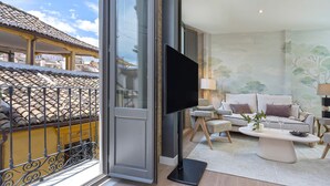 A spacious living room with a large flat-screen TV, a comfortable sofa set, and a balcony with a tiled roof.