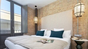 A modern hotel room with a large bed, a brick wall, and a balcony.