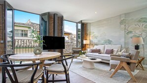 A modern living room with a large window, a round wooden table, a sofa, and a TV.