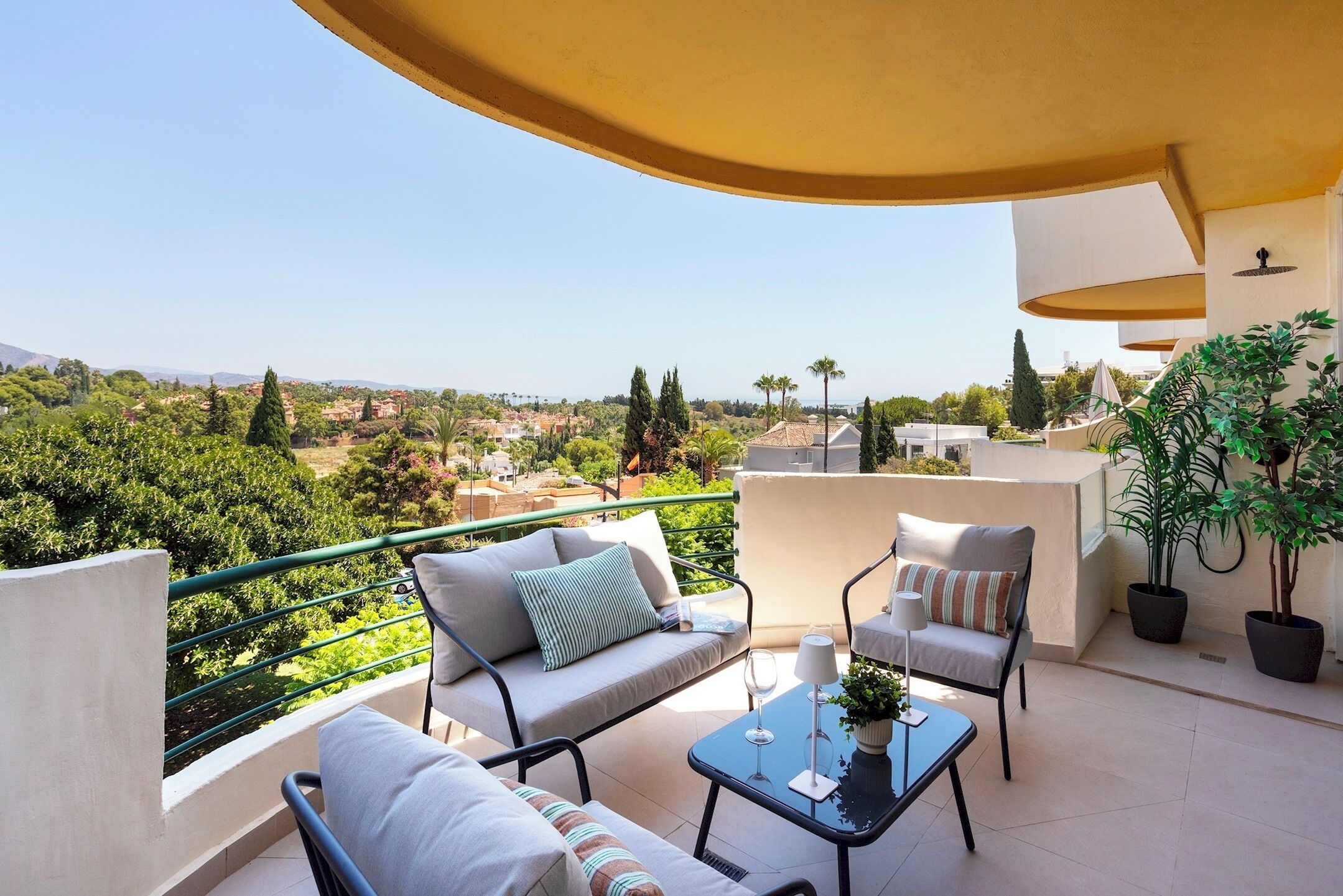 A balcony with a sofa, chairs, a table, and potted plants.