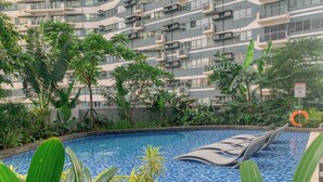 A swimming pool with a tiled edge, surrounded by lush greenery and a multi-story building in the background. - Room-makati Penthouse Studio With City V (Makati)