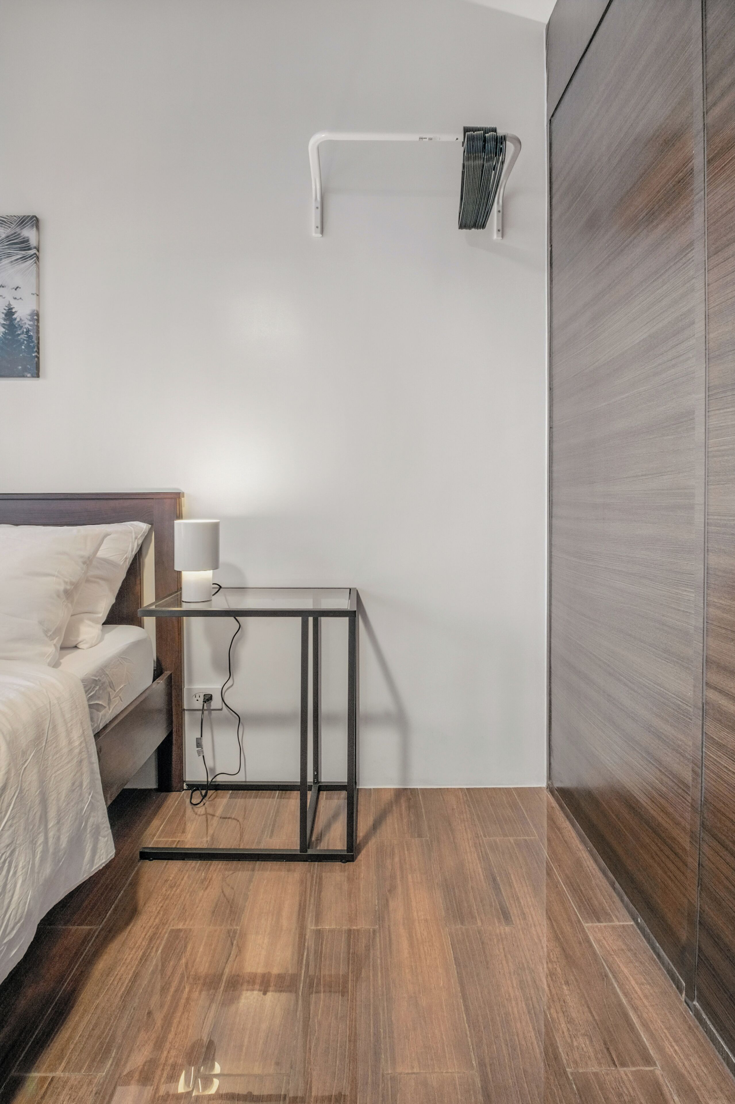 Een moderne slaapkamer met een bed, nachtkastje, lamp en een houten garderobe.