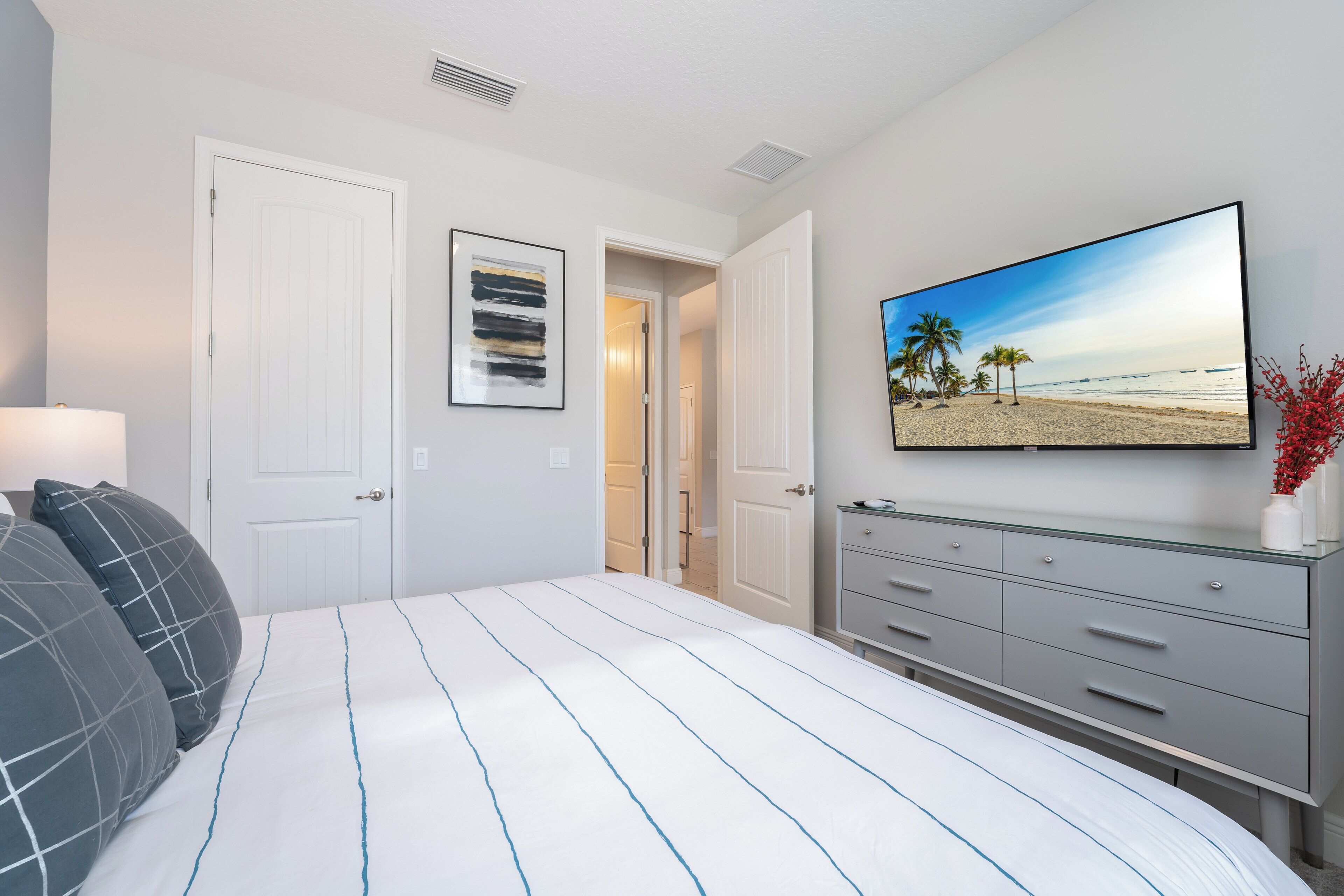 Une chambre à coucher comprenant un lit, une commode, un tableau encadré et une porte donnant sur une autre pièce.