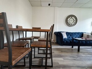 Ett rum med en blå soffa, träbord och stolar, en rund väggklocka och ett vitt tak.