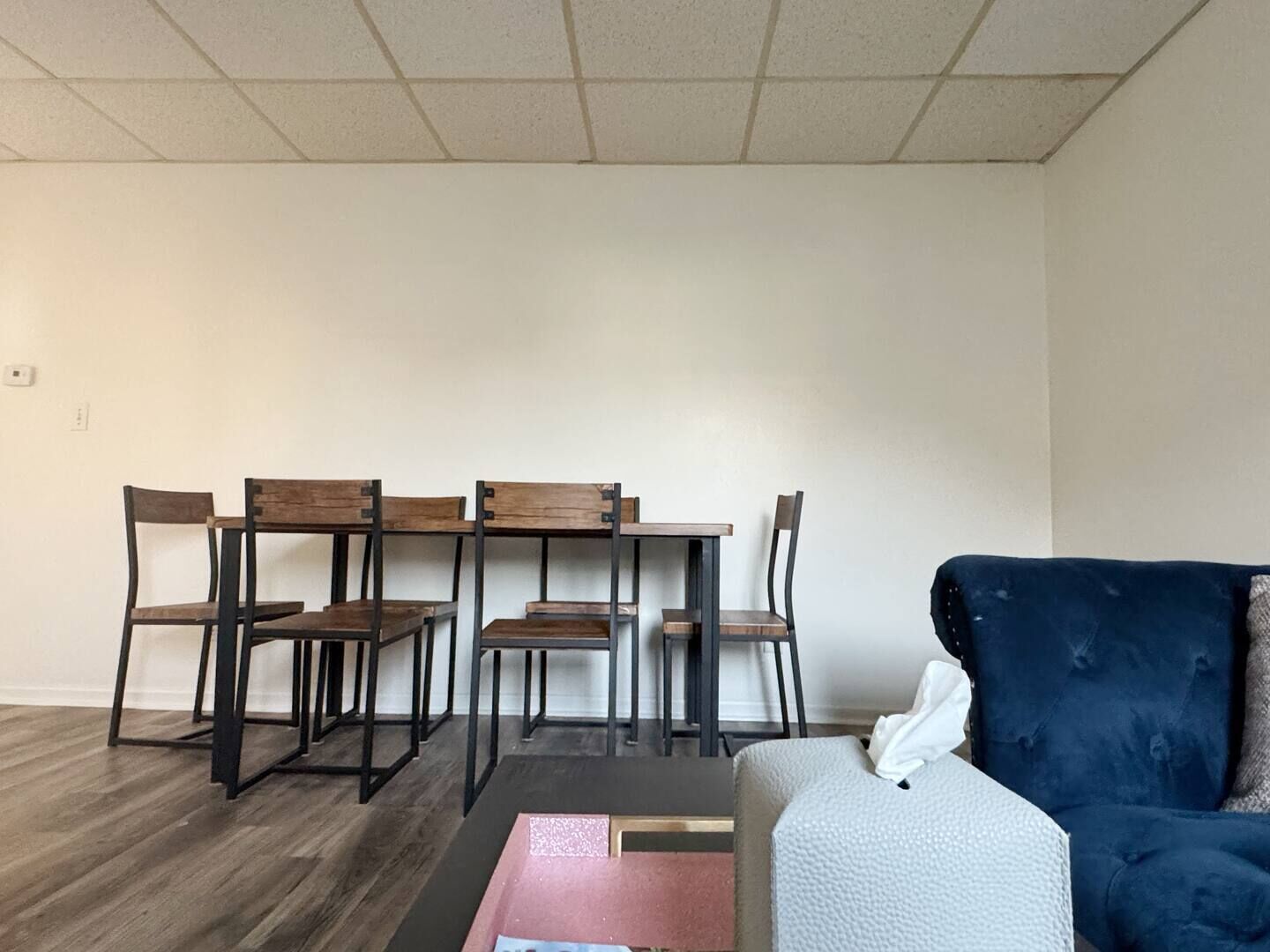 A room with a dark wooden dining table and chairs, a blue sofa, and a small white table.