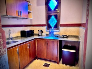 A compact kitchen with wooden cabinets, a microwave, a coffee maker, and a trash bin. - El Juneina Boutique Villas (Luxor)