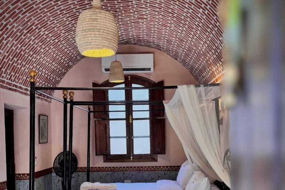 A four-poster bed with a canopy, a wooden nightstand, and a window with wooden shutters.