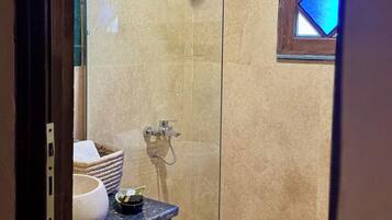 A glass-enclosed shower with a handheld showerhead, a small sink with a soap dish, and a decorative window with blue-tinted glass.