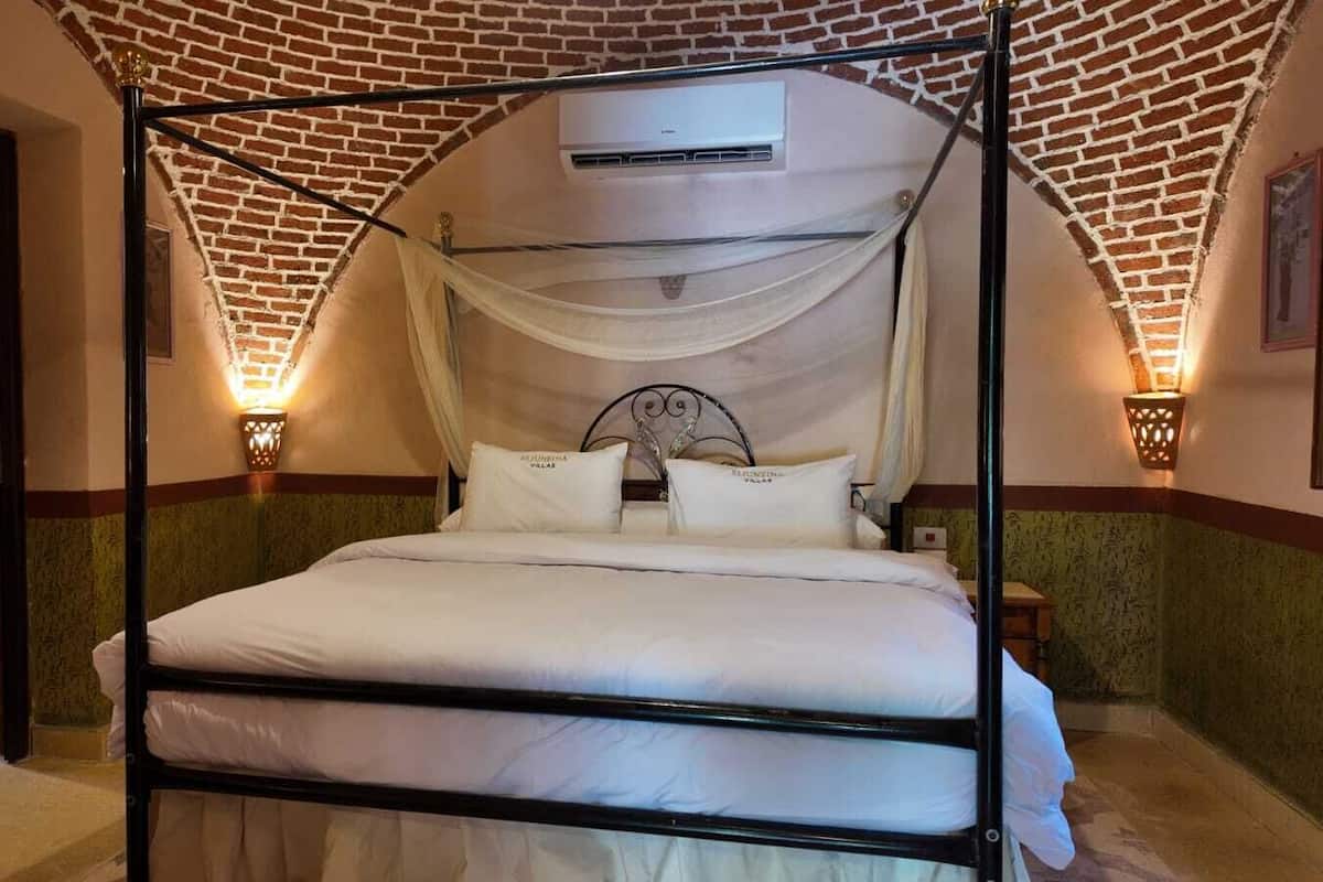A four-poster bed with a canopy, a wall-mounted air conditioner, and two wall sconces.