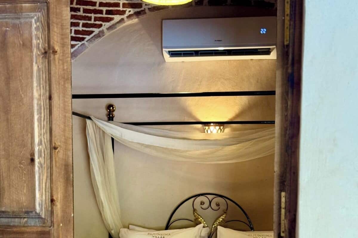 A single bed with a canopy, a bedside table, and an air conditioning unit above it.