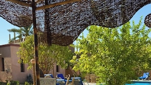 An outdoor dining area with a table set for a meal, surrounded by lounge chairs and a pool in the background. - El Juneina Villas - Luxury Boutique Villas Near Valley of the Kings (Luxor)