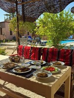 Un área de comedor al aire libre con una mesa lista para una comida, rodeada de sillones de descanso y una piscina al fondo.