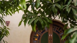 A wooden double door with a decorative arch design, a small wall-mounted emblem, and a textured mat at the entrance. - El Juneina Villas - Luxury Boutique Villas Near Valley of the Kings (Luxor)