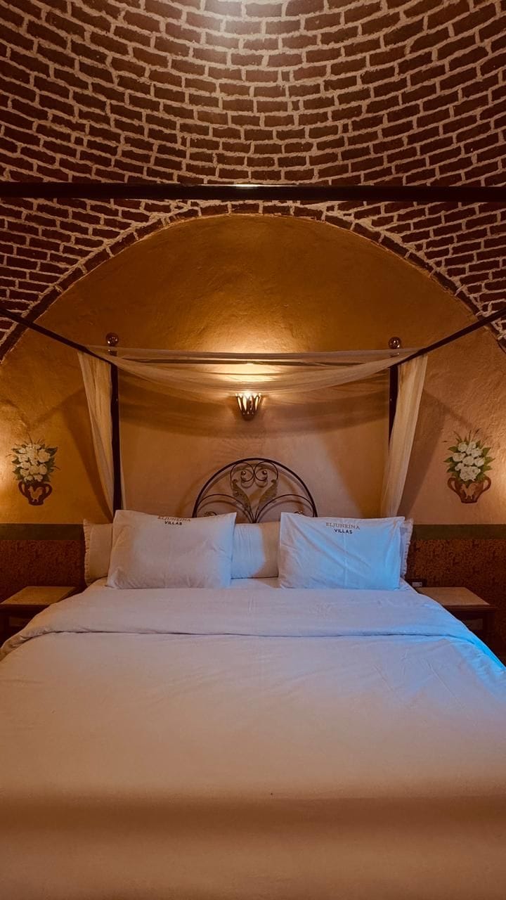 Una cama con dosel, una pared con diseño de ladrillo y dos lámparas fijadas a la pared.