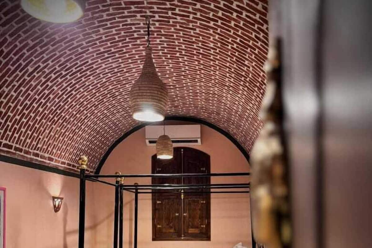 A room with a brick ceiling, a bed with white bedding, and a patterned floor.