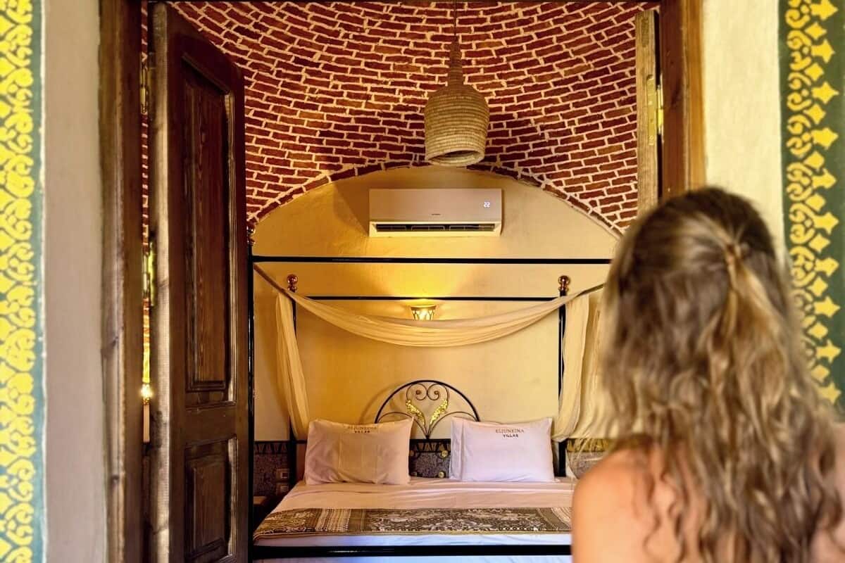 A room with a bed, a hanging light fixture, and a wall-mounted air conditioning unit.