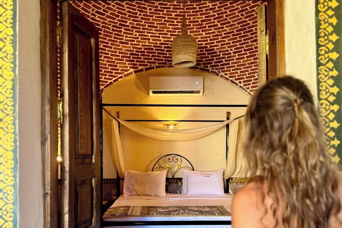 A room with a bed, a hanging light fixture, and a wall-mounted air conditioning unit.