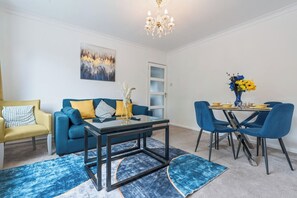 En moderne stue med en blå sofa, en gul lænestol og et spisebord med blå stole.