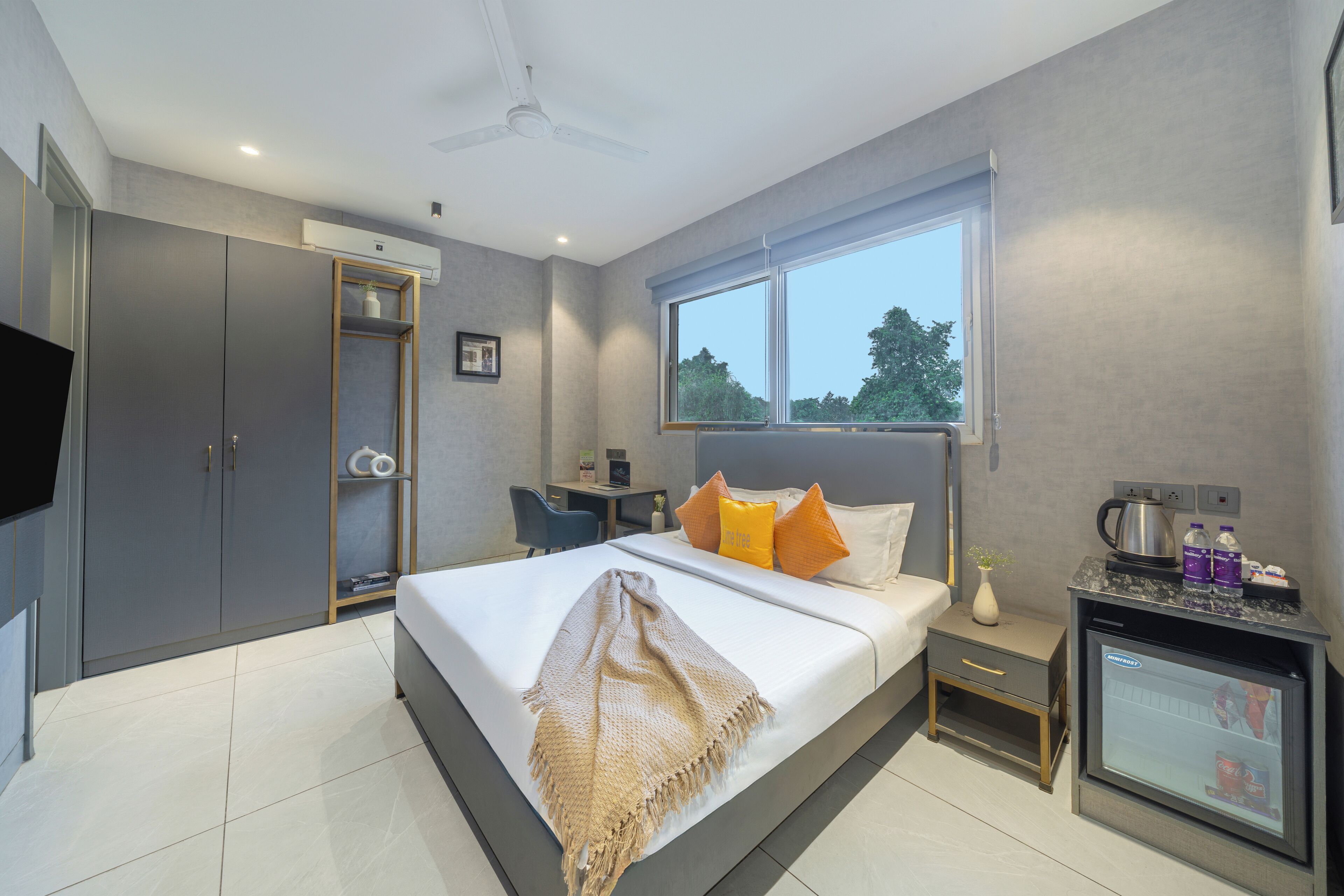 A modern hotel room with a bed, a desk, a mini-fridge, a TV, and a wardrobe.