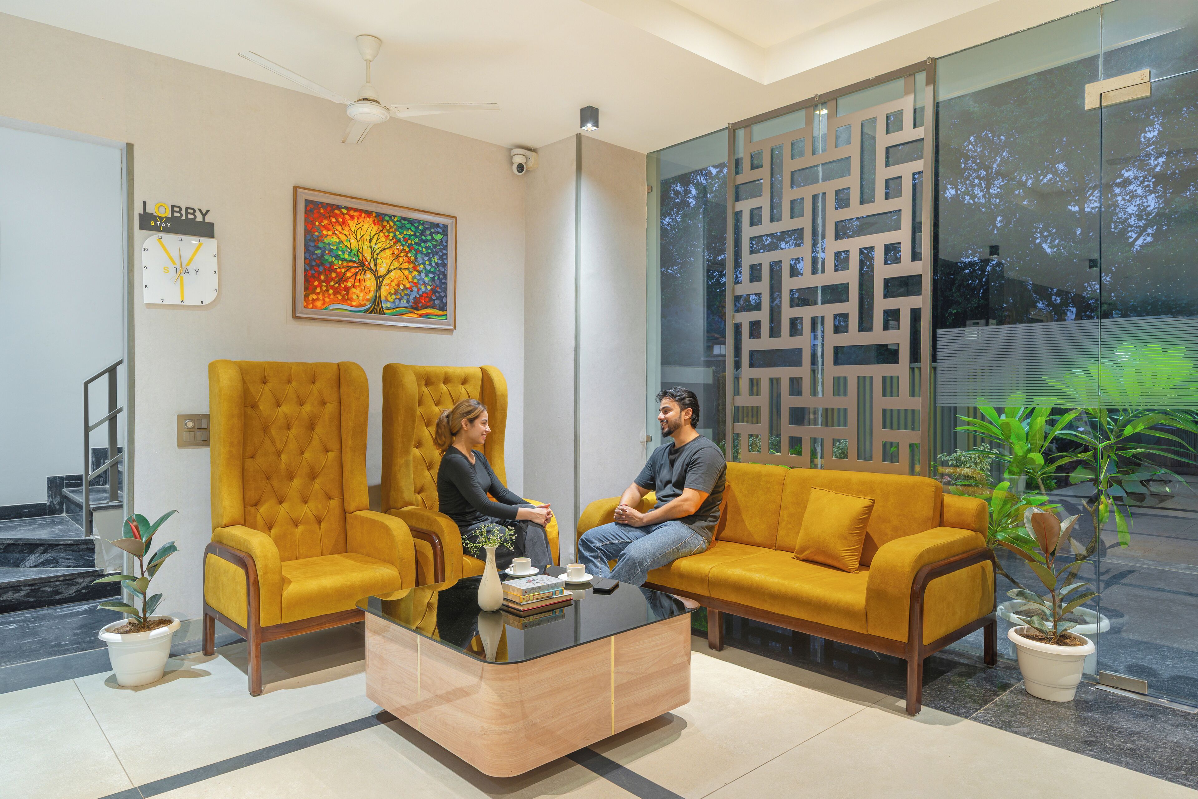 A lobby with a modern design, featuring a yellow sofa, a glass coffee table, and a decorative wall piece.