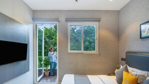 Une chambre moderne dotée d’un grand lit, d’un téléviseur à écran plat et d’une porte-fenêtre coulissante donnant sur un balcon.