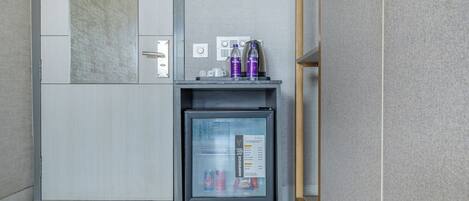 A minibar with a glass door, containing a water bottle, a can, and a small box.