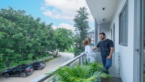 Un balcon donnant sur une route et des voitures garées, entouré de verdure.