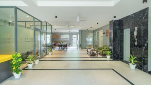Un hall d’hôtel moderne avec des murs en verre, un espace repas et un comptoir d’accueil.