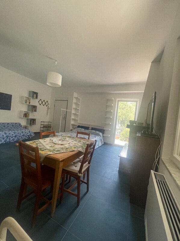 A spacious living area with a dining table, chairs, a sofa, and built-in shelving. - CASA AZZURRA Nice one-room apartment with terrace in Cilento. Pet friendly (Castellabate)