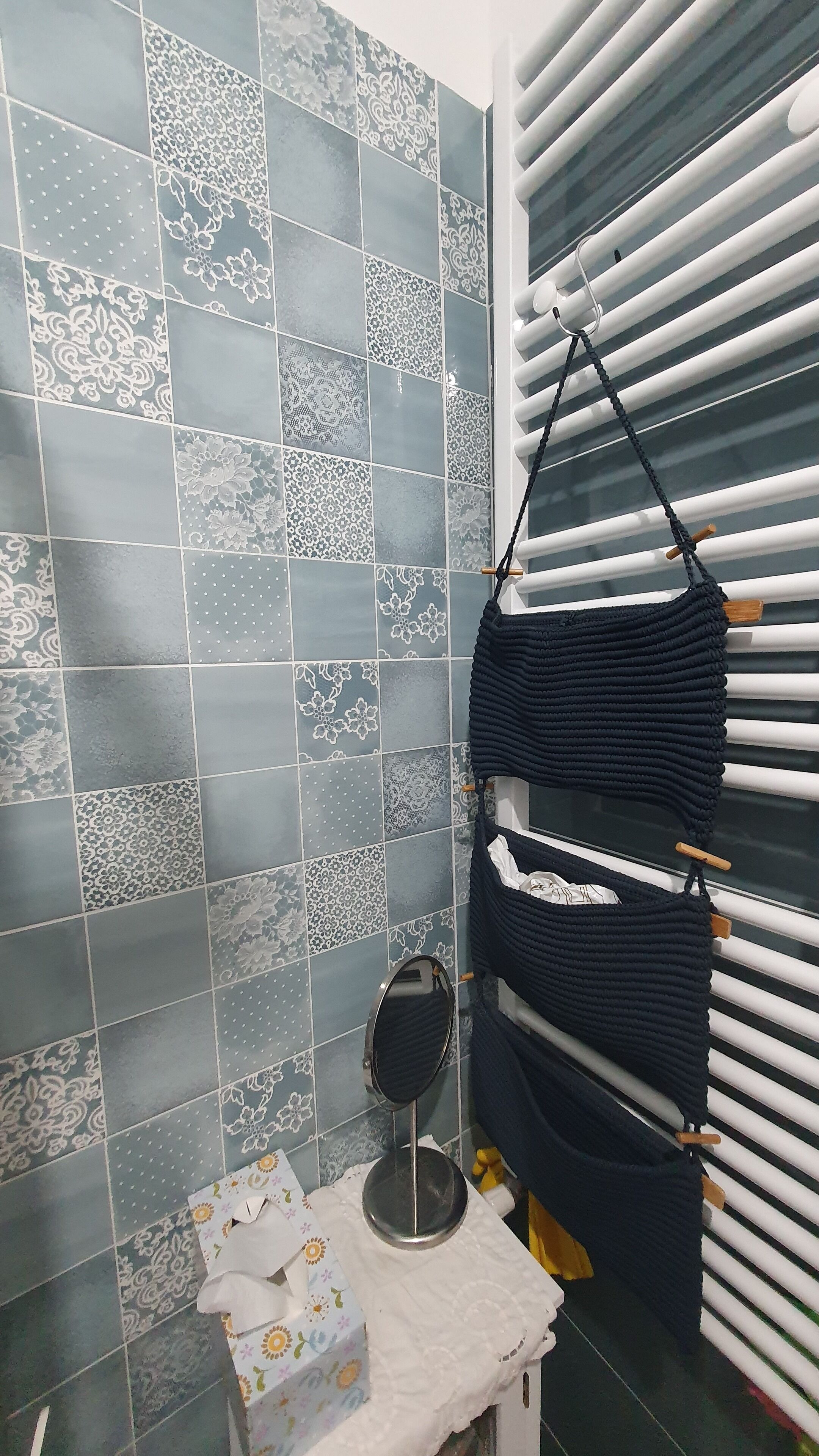 Een badkamer met tegelwerk, een handdoekhouder, een klein spiegel en een zakdoos.