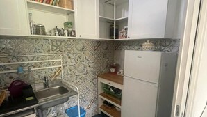 Ett kompakt kök med vita skåp, en diskho i rostfritt stål och ett litet kylskåp.
