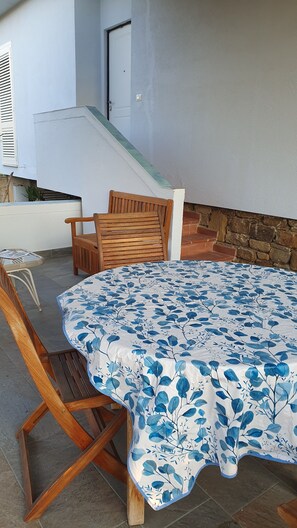 A patio area with a round table covered by a floral tablecloth, two wooden chairs, and a stone wall. - CASA AZZURRA Nice one-room apartment with terrace in Cilento. Pet friendly (Castellabate)