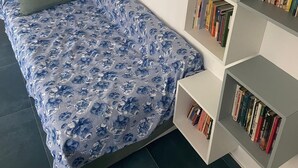 Ett litet sovrum med en enkelsäng, en bokhylla och en tavla på väggen.