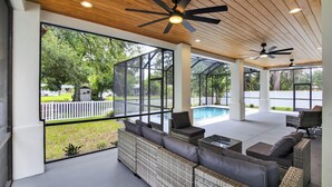 Ein überdachter Außenbereich mit Korbmöbeln und Deckenventilatoren, mit Blick auf einen Swimmingpool und Grünflächen.