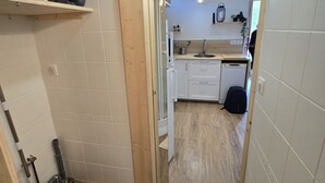 Ein schmaler Flur führt zu einer Küche mit weißen Schränken, einem Spülbecken und einem Holzboden.