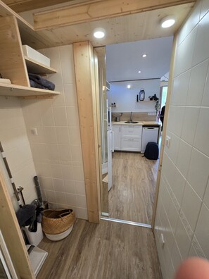 Een smalle gang die leidt naar een keuken met witte kastjes, een spoelbak en een houten vloer.