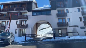 Ein mehrstöckiges Hotel mit Balkonen, im Hintergrund eine Skipiste und ein verschneiter Eingangsbereich.