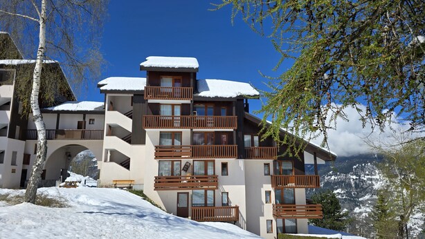 Ein mehrstöckiges Hotel mit Balkonen, schneebedeckten Dächern und einer Bergkulisse.