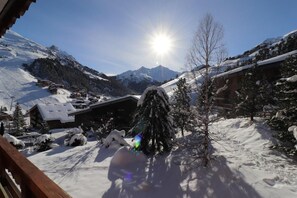 A snow-covered mountain landscape with a wooden cabin and a tree in the foreground.