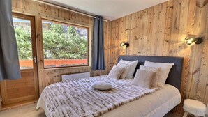 Un dormitorio con pared de madera, una cama grande con una colcha blanca, dos almohadas y un taburete pequeño.