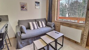 Un cuarto acogedor con un sofá gris, dos almohadas, una mesita y una ventana con vista a los árboles.