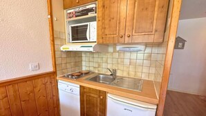 A compact kitchen with wooden cabinets, a microwave, a sink, and a dishwasher.