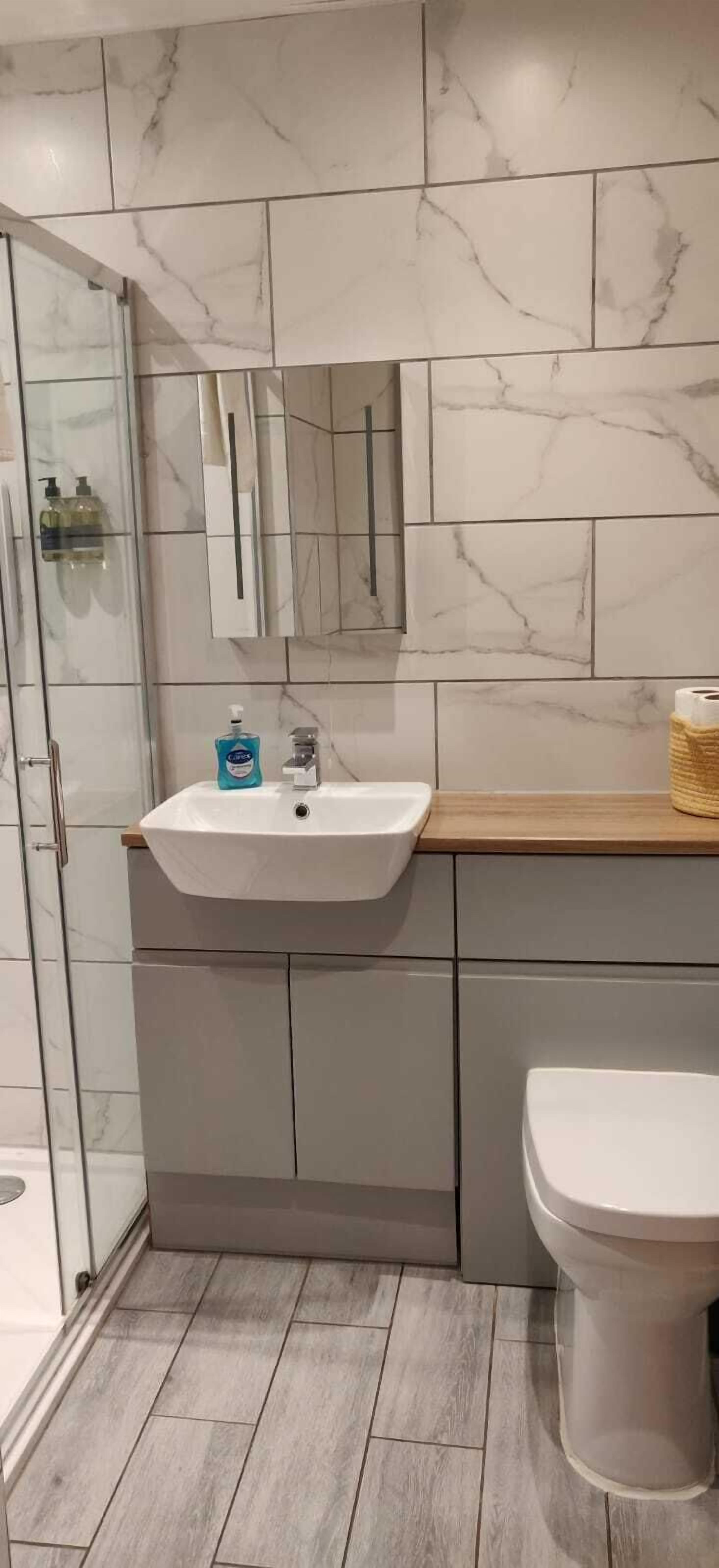 Ein modernes Badezimmer mit Marmorfliesen, einem weißen Waschbecken mit Spiegel darüber und einer Toilette.