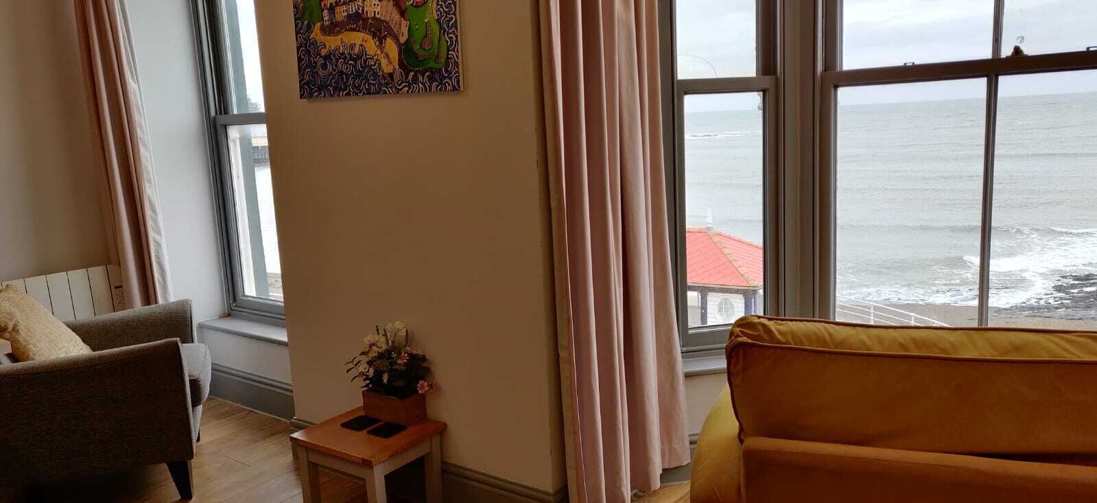 Una stanza con una grande finestra vista mare, un tavolino con un vaso di fiori e due divani.