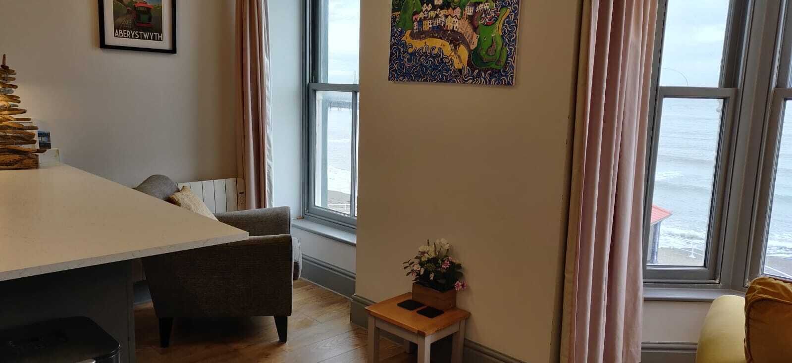 A room with a dining table, a chair, a small table with a flower vase, and a wall with a colorful map.