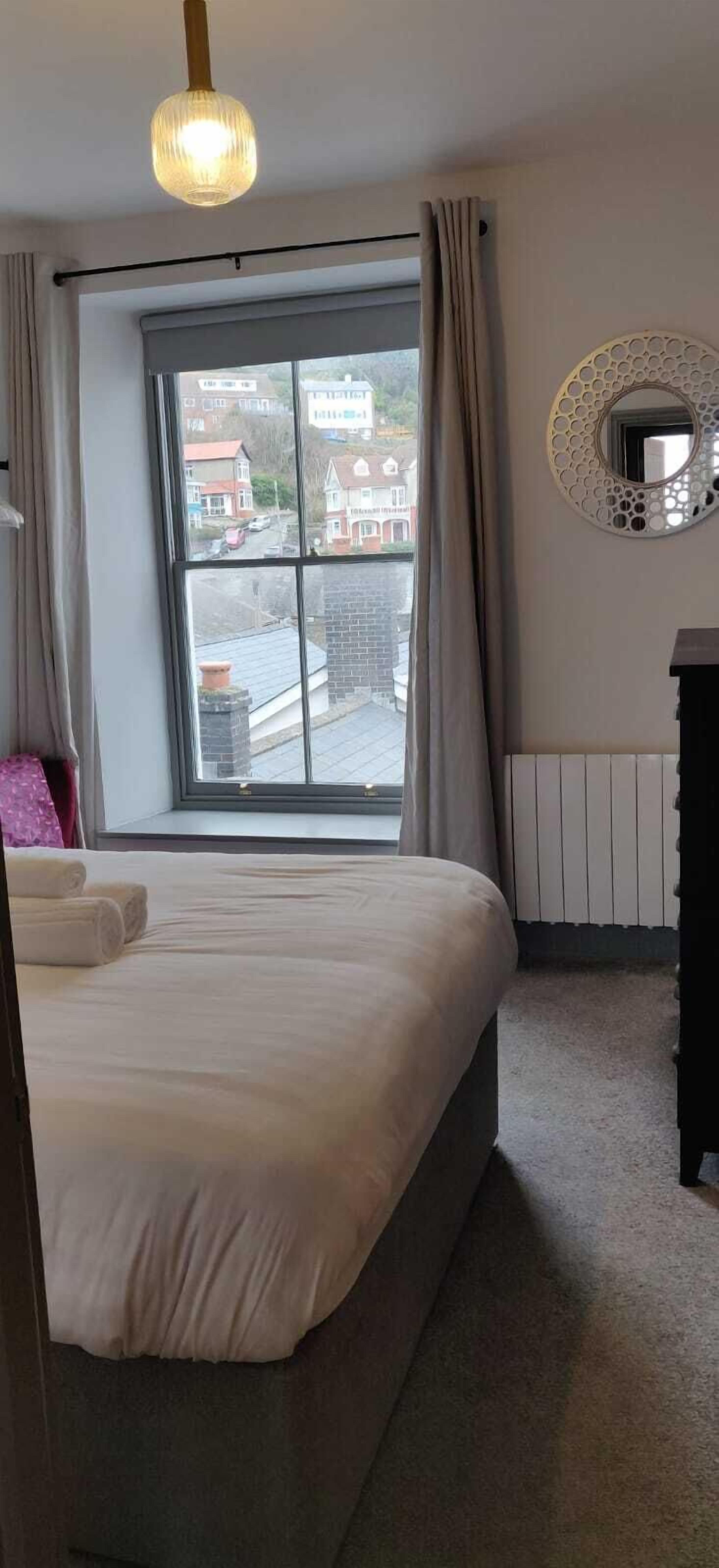 Una camera da letto con un letto, una finestra con tende, un termosifone e uno specchio fissato al muro.