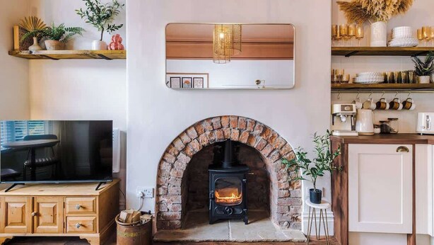 A cozy living room with a fireplace, wooden shelves, a television, and a kitchen area.