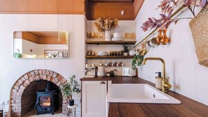 A kitchen with a brick fireplace, wooden shelves, and a white sink.