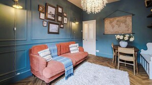 A room with a blue wall, a red sofa, a chandelier, framed pictures, a map, and a white rug.