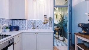 A kitchen with white cabinets, a blue patterned backsplash, a coffee machine, and a potted plant.
